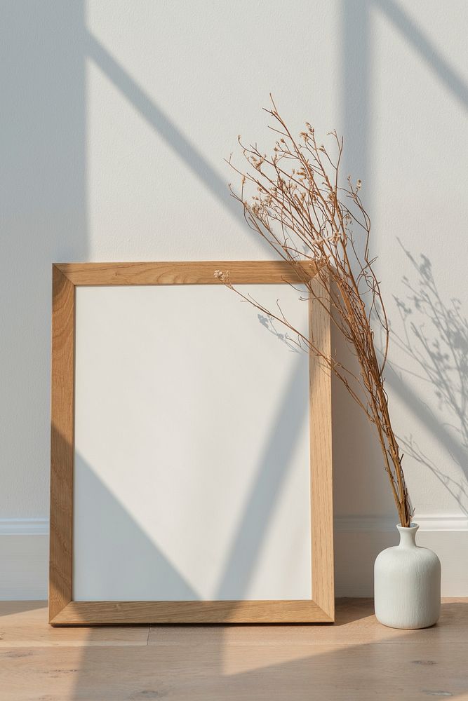 Dried white statice flower in a white vase by an empty wooden frame on a wooden floor