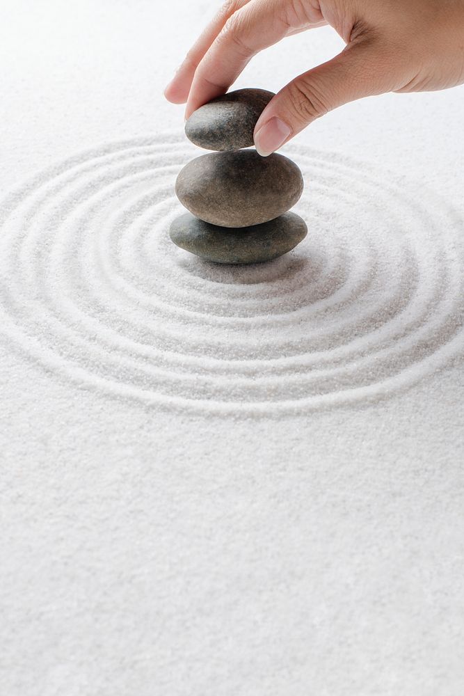 Hand stacking zen stones on the sand wellness background