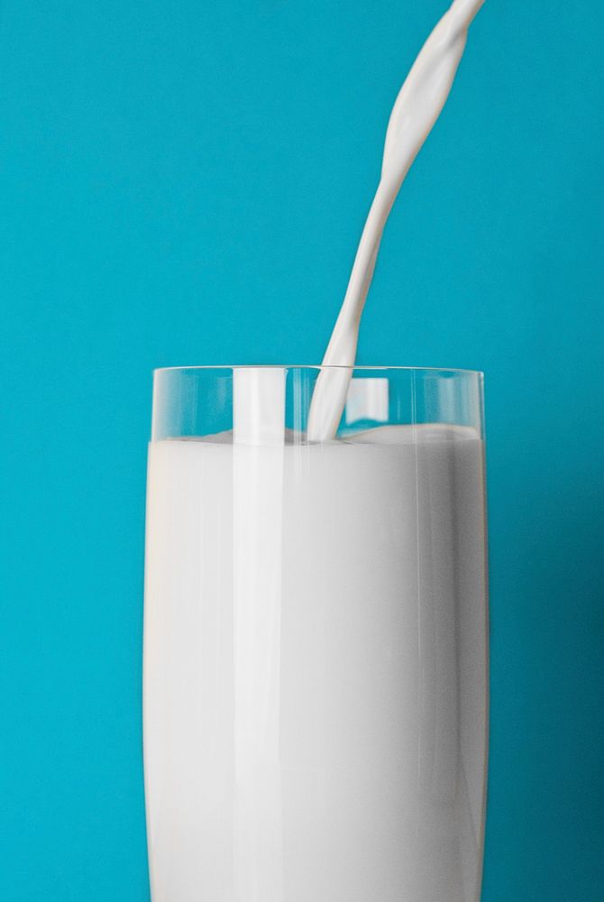 Free pouring milk into glass blue background photo, public domain beverage CC0 image.