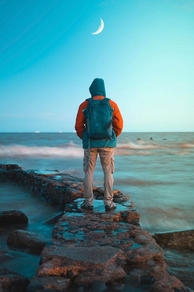 Man standing on rocks facing sea, free public domain CC0 photo.