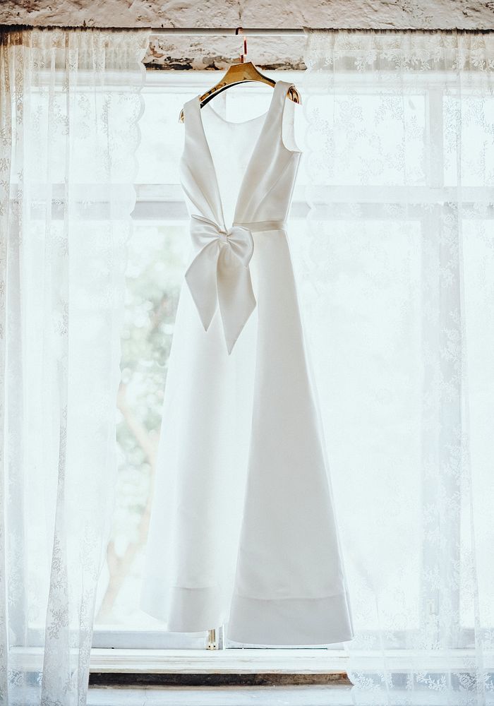 Wedding dress hanging by window, aesthetic photo
