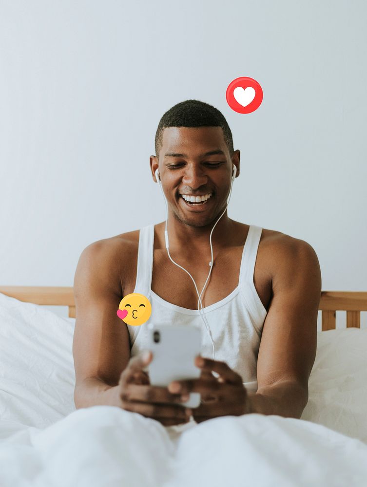 Cheerful black man in bed playing with his phone
