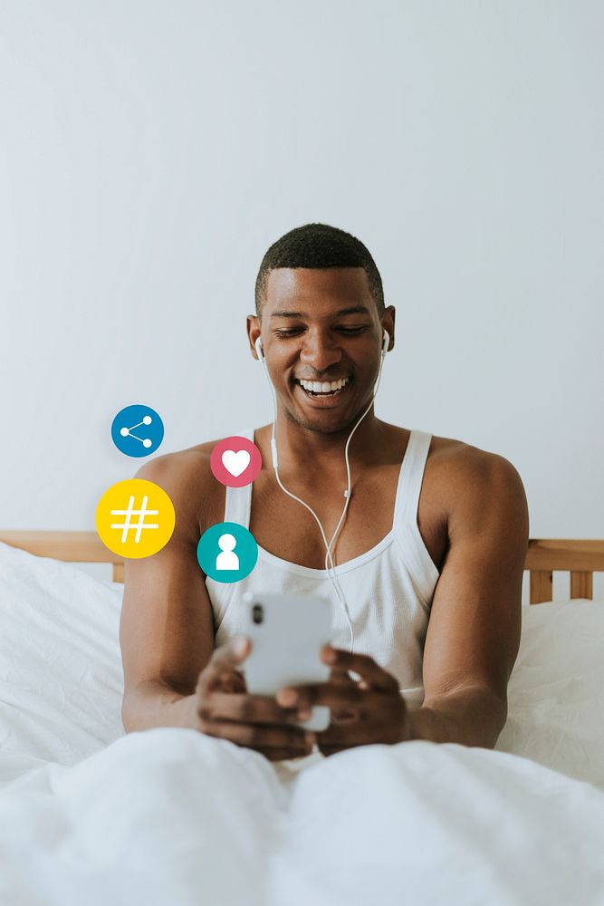 Cheerful man playing on his mobile phone in bed