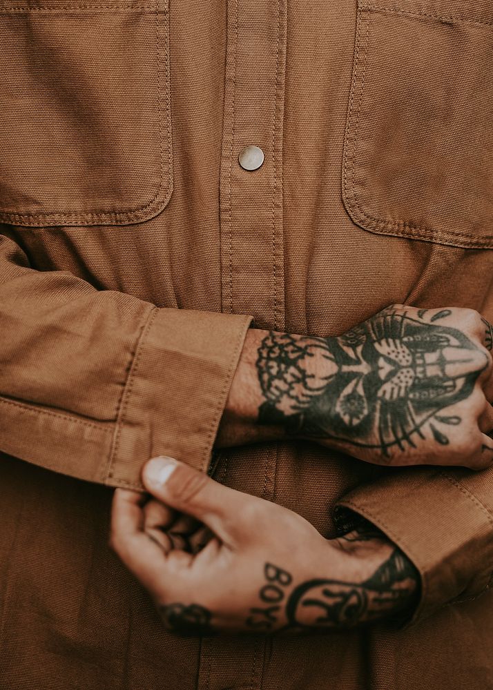 Tattooed man buttoning brown shirt