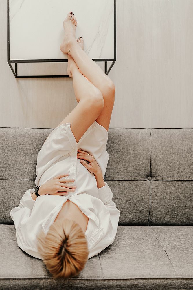 Pregnant blond-haired woman relaxing on a gray sofa