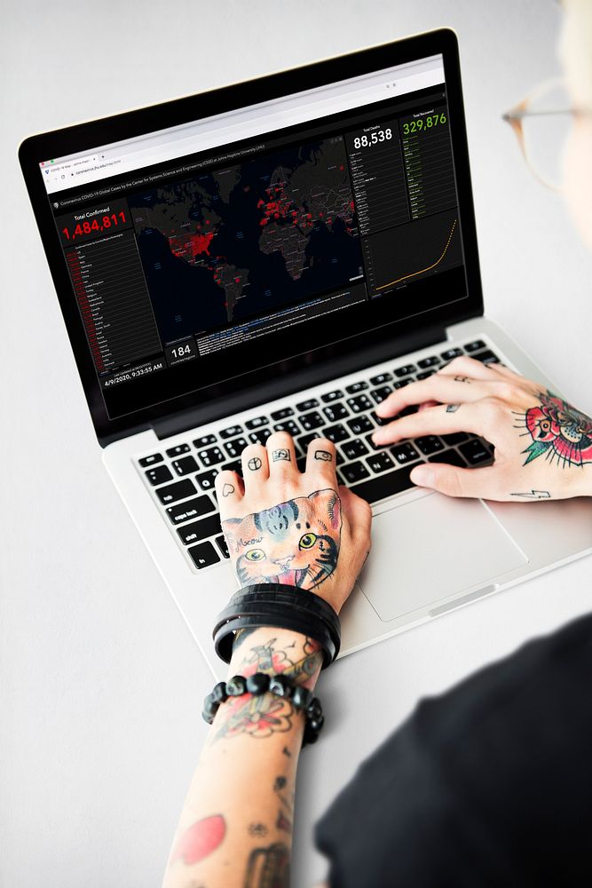 Tattooed man reading the report of coronavirus cases from a laptop mockup with editorial graphic from…
