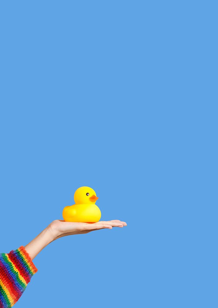 Hand holding a yellow rubber duck on blue background
