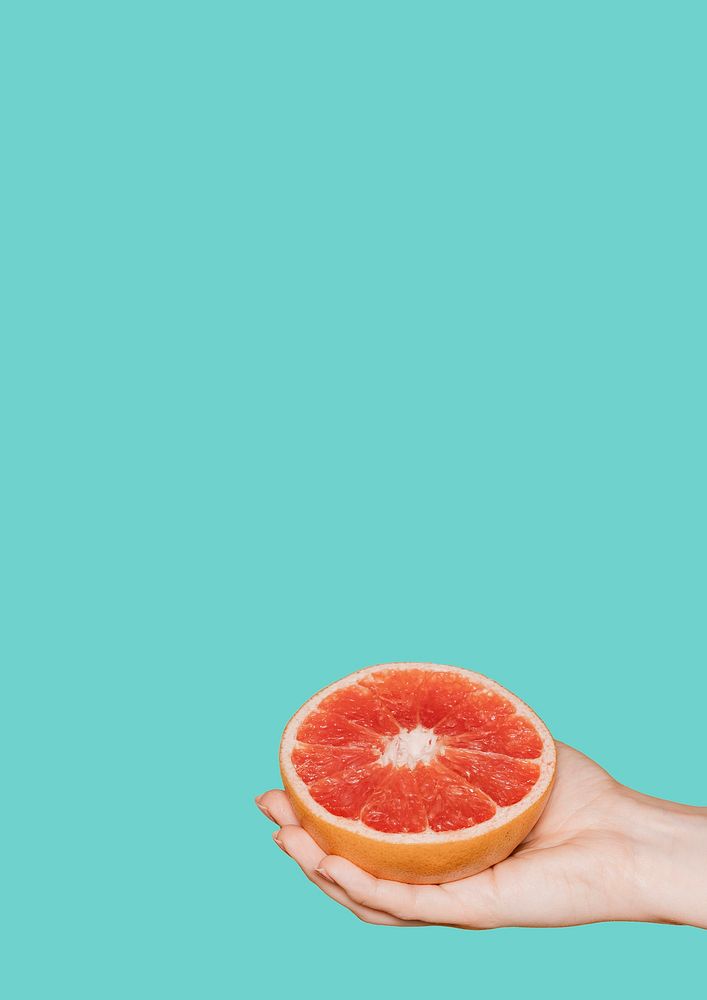 Hand holding a fresh grapefruit on a green background