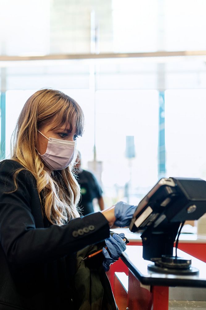 Woman in a face mask wearing latex gloves while purchasing at a self-checkout in a supermarket during coronavirus quarantine