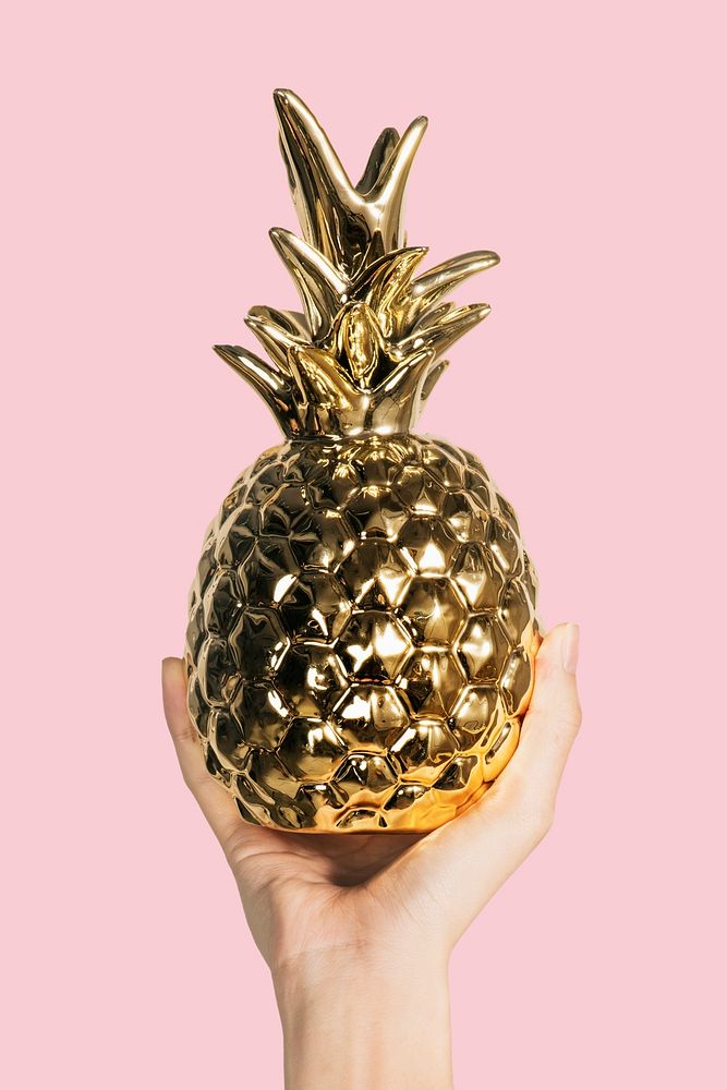 Hand showing a gold pineapple cup on a pink background