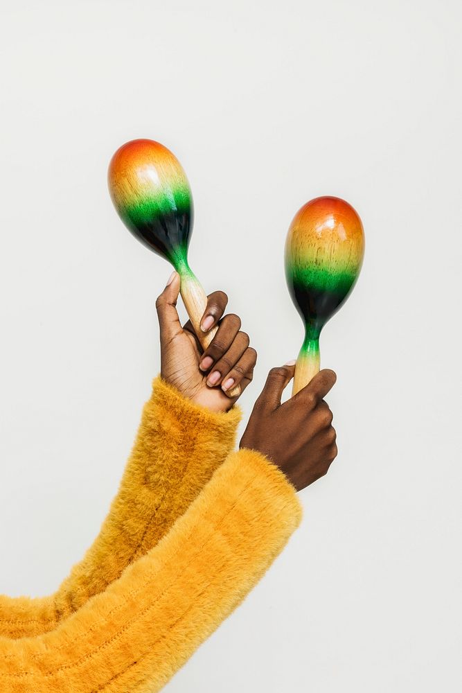 Black hands in a yellow sweater holding maracas isolated on a gray background