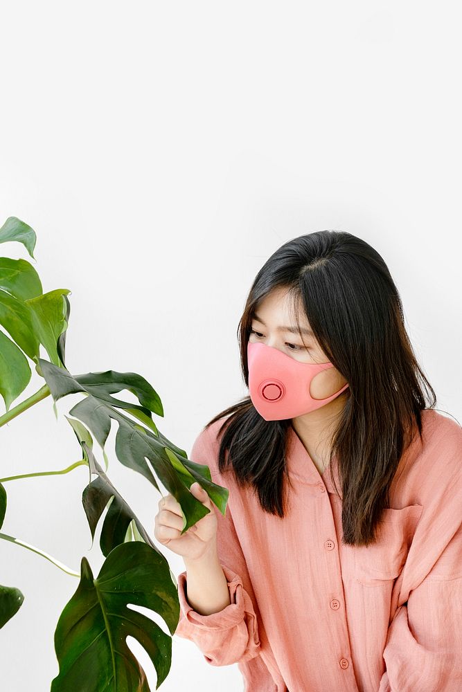 Asian woman wearing a mask standing next to a monstera plant