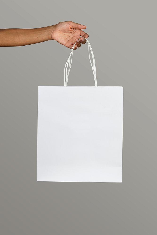 Black woman holding a white paper bag mockup on a gray background