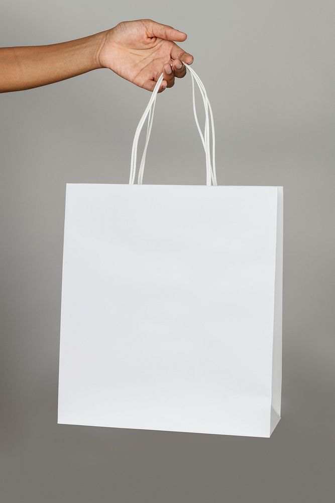 Black woman holding a white paper bag mockup on a gray background