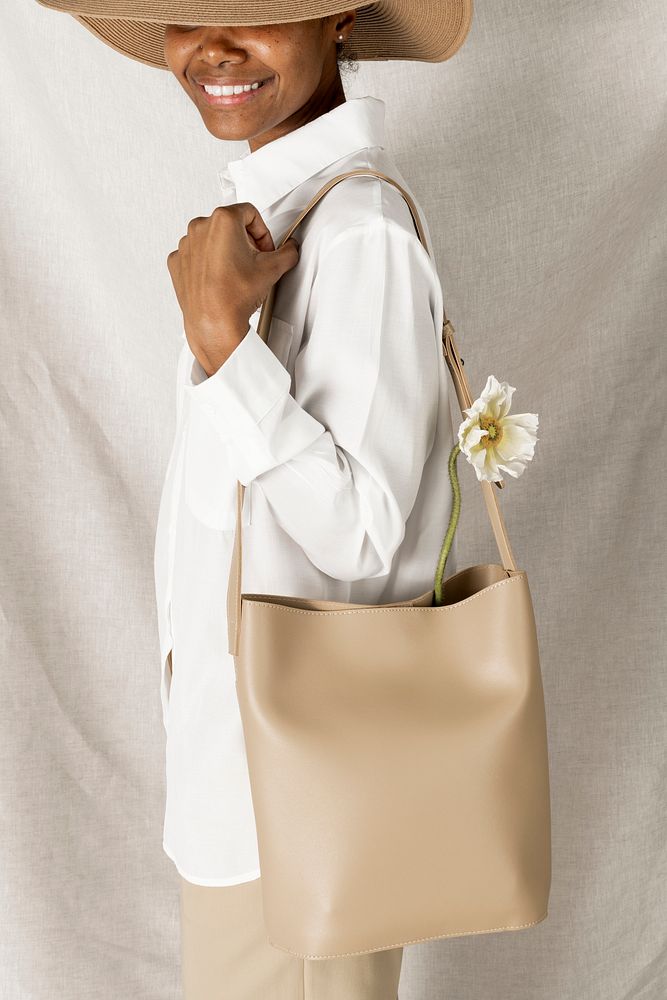 Happy black woman with a white poppy flower in her cream bucket bag