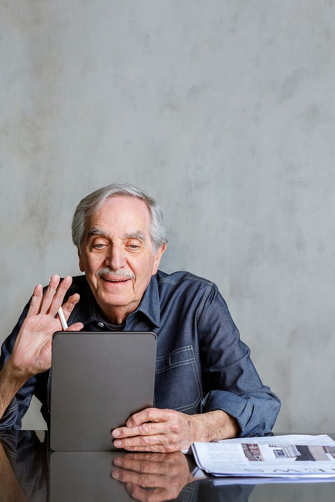 Senior man making video call from tablet computer with a mug and newspaper on the table