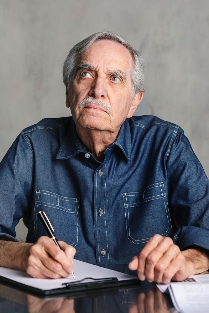 Thoughtful senior man writing on a paper clipboard 