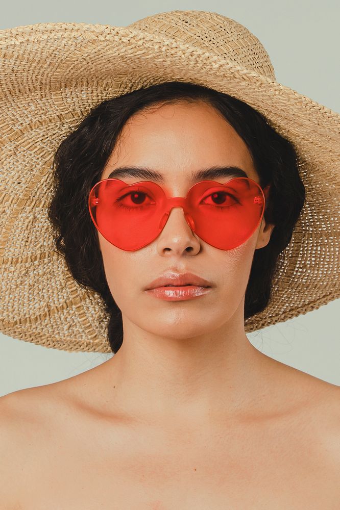 Bare chested woman wearing a big round hat and red vintage heart-shaped sunglasses