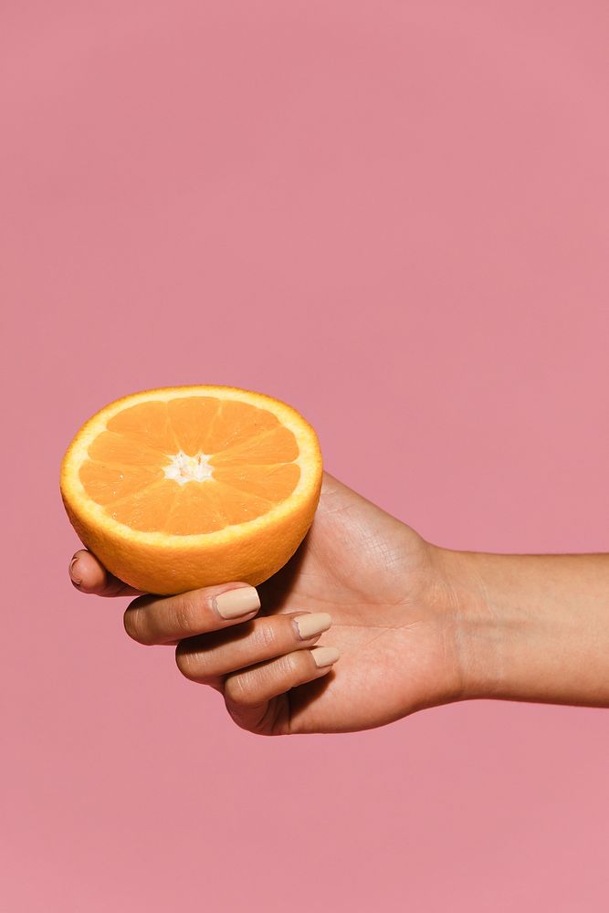 Woman holding half an orange against a pink background 