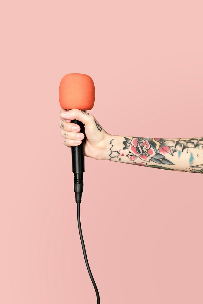 Tattooed hand holding a microphone with light pink background