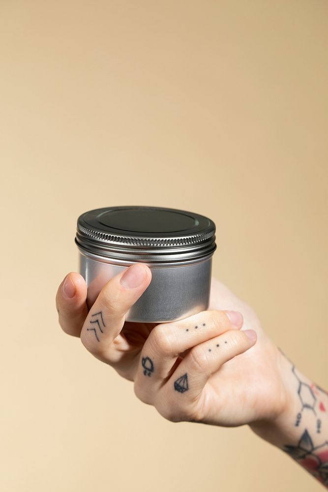 Tattooed hand holding an unlabeled face cream jar 