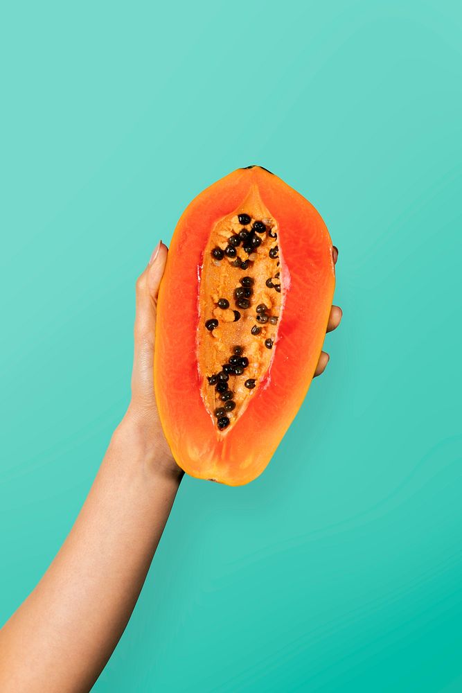 Hand showing a half of ripe papaya with a  cyan wall