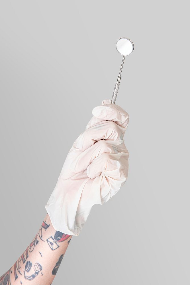 Tattooed hand in a white glove holding a dentist's mirror mockup