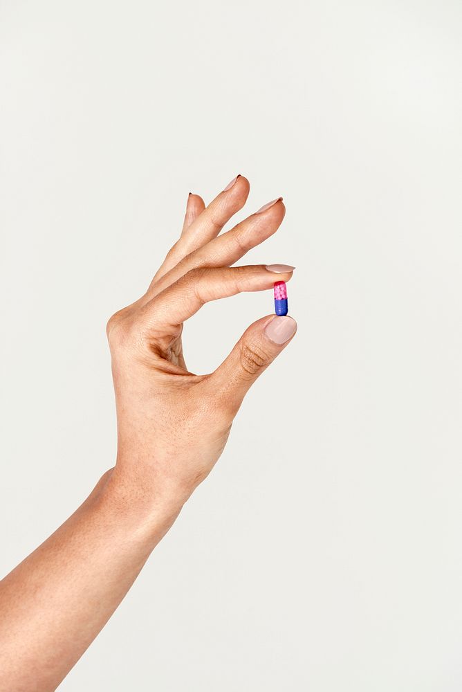 Feminine hand holding a pink and blue pill