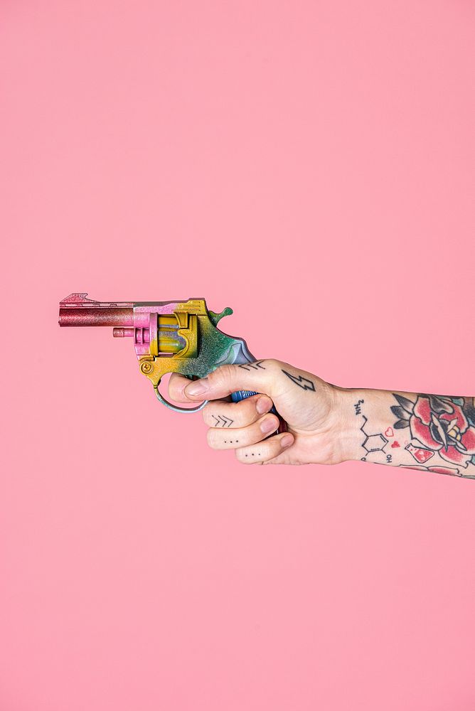 Tattooed hand holding a rainbow toy gun