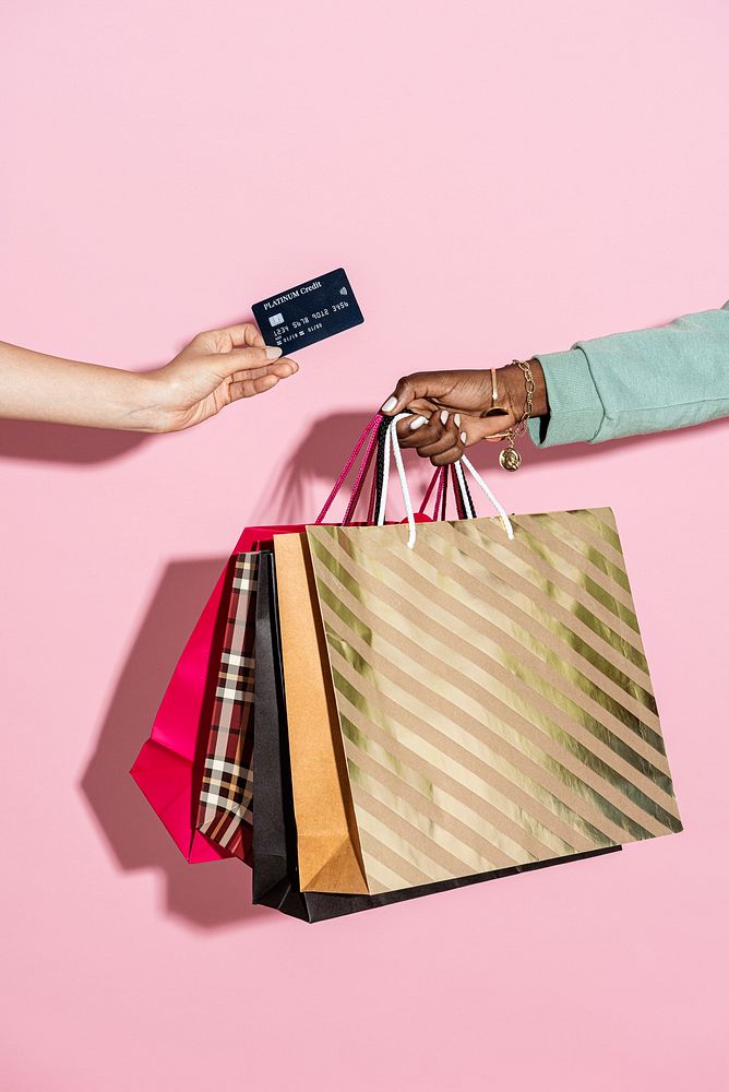 Woman with shopping bags and a credit card against a pink background