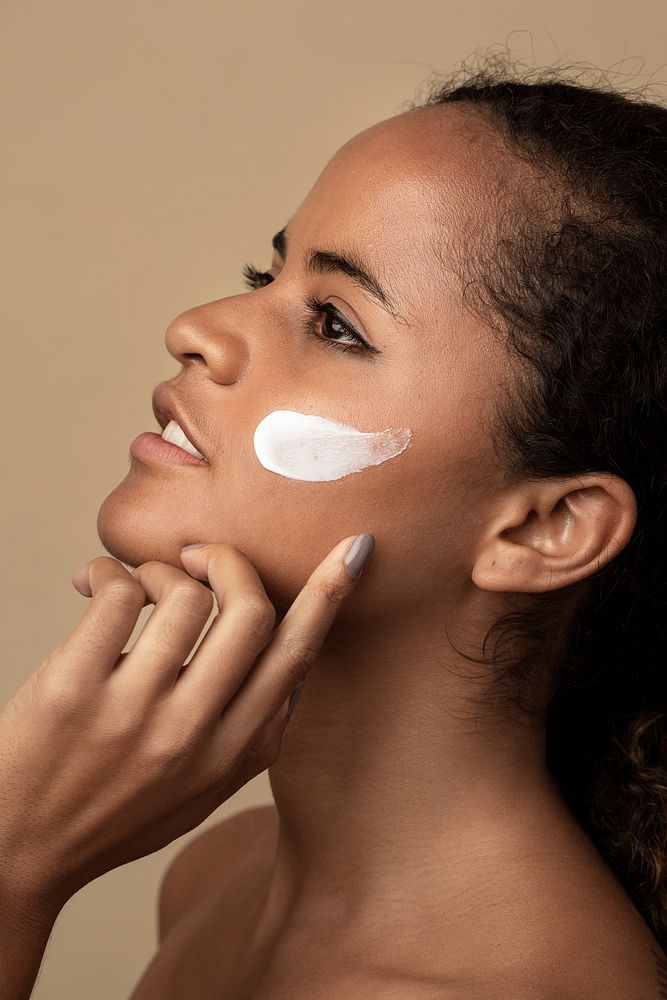 Beautiful African American woman using a moisturizing cream for skincare routine