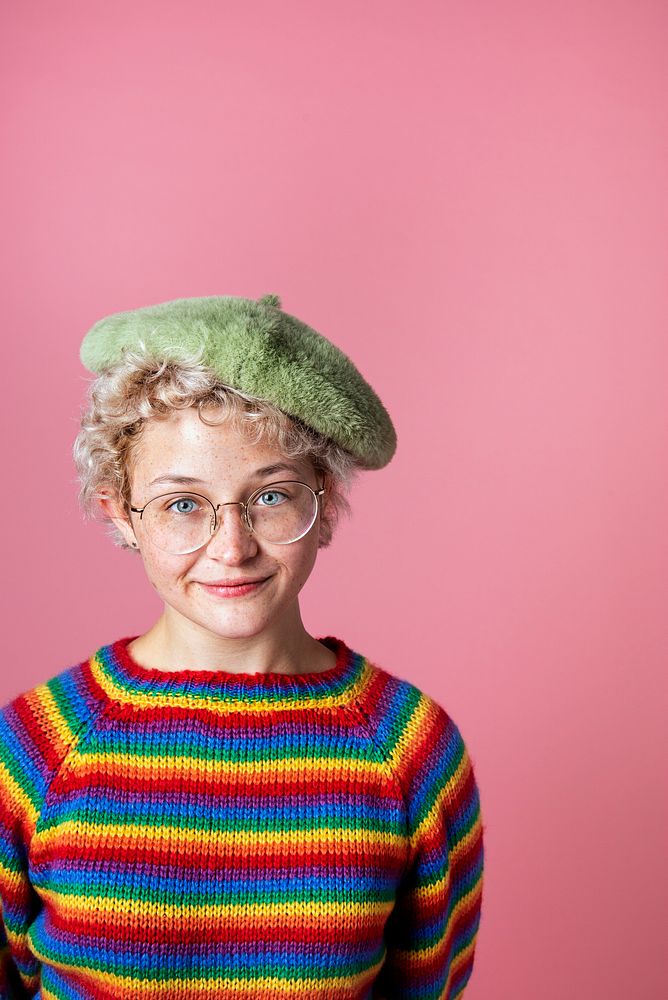 Cheerful girl wearing rainbow sweater and green beret in a pink background