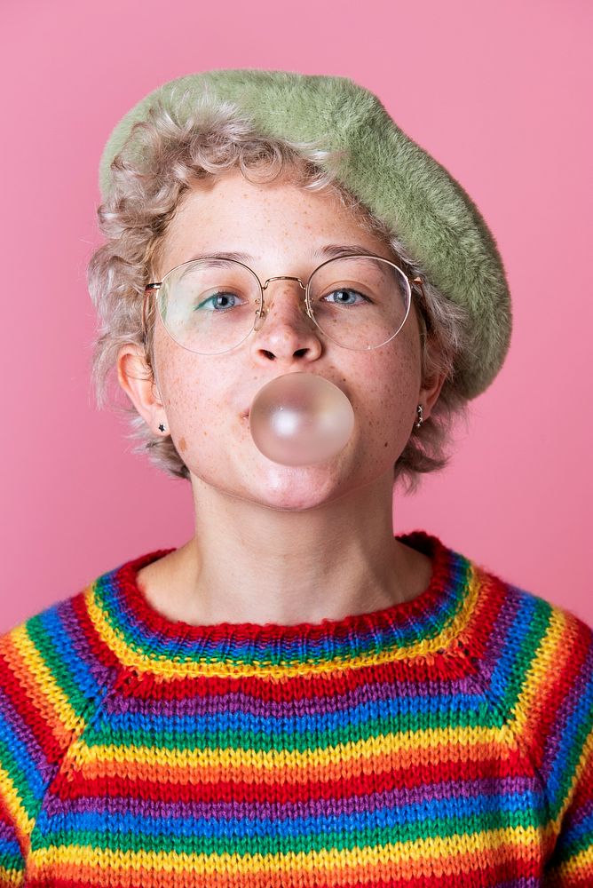 Cheerful girl wearing a green beret and a rainbow sweater chewing a bubble gum