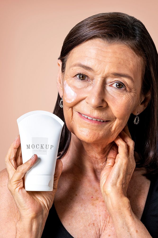 Senior woman holding a white face cream tube mockup