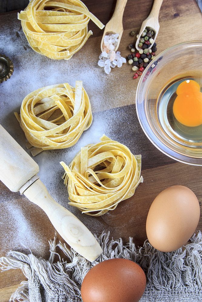 This is a table with fresh pasta, eggs and rolling pin. Original public domain image from Wikimedia Commons
