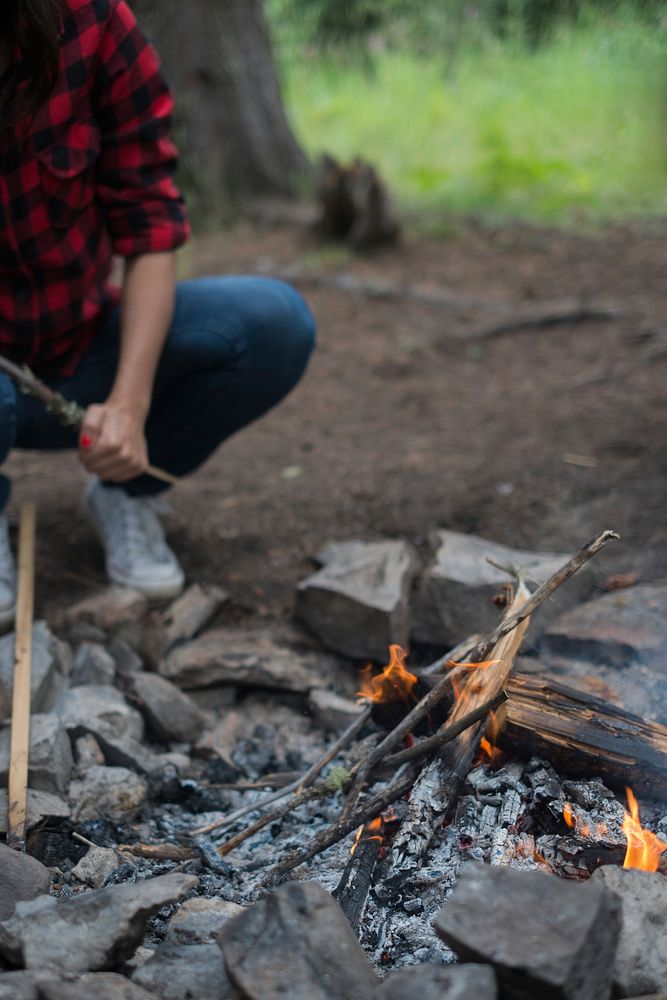 A camper wearing flannel and jean tending to a fire while camping. Original public domain image from Wikimedia Commons