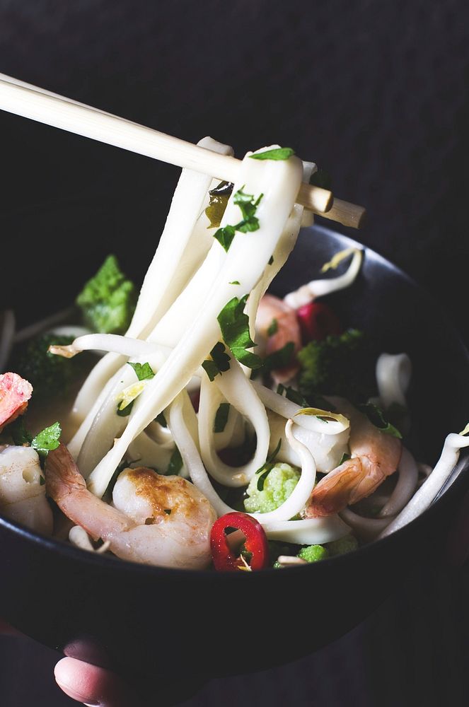 Chopsticks pick up noodles from a bowl full of shrimp and herbs. Original public domain image from Wikimedia Commons