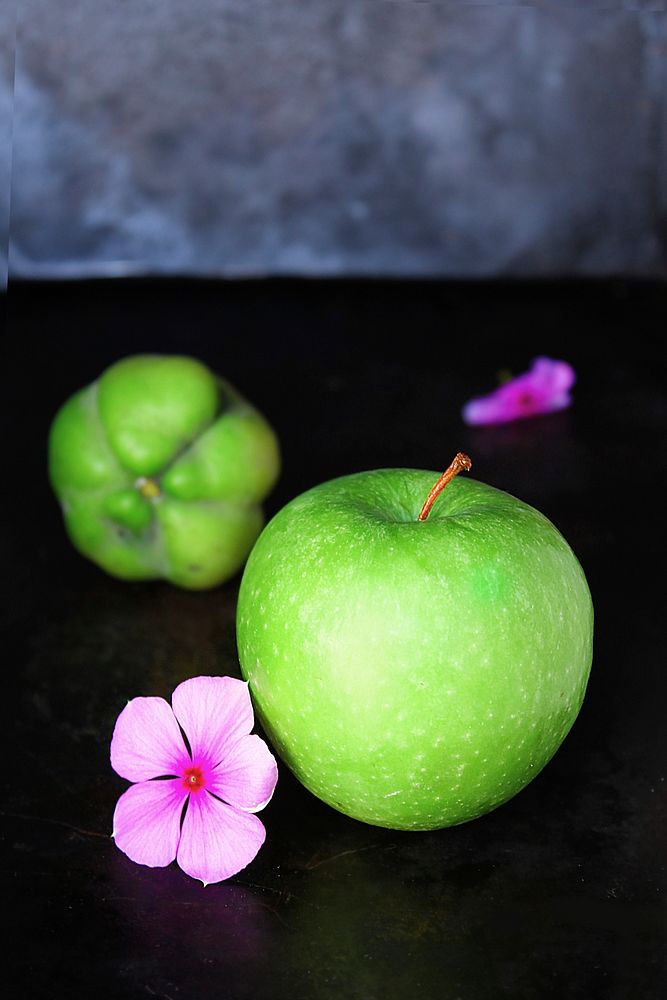 Fresh green granny smith apple next to purple flowers and a green fruit. Original public domain image from Wikimedia Commons