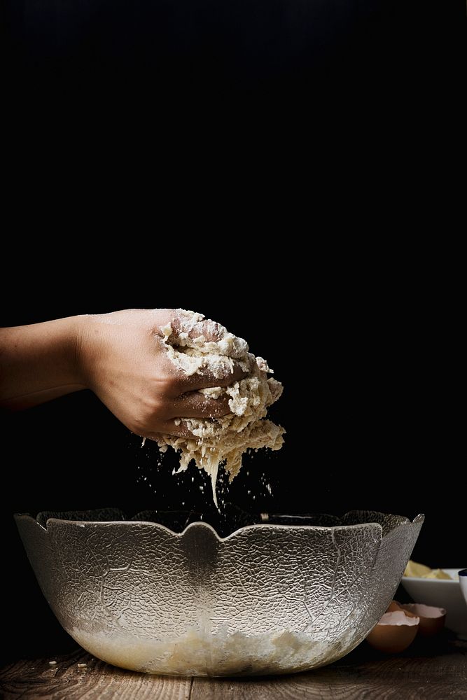 A person's hand kneading dough over a glass bowl. Original public domain image from Wikimedia Commons