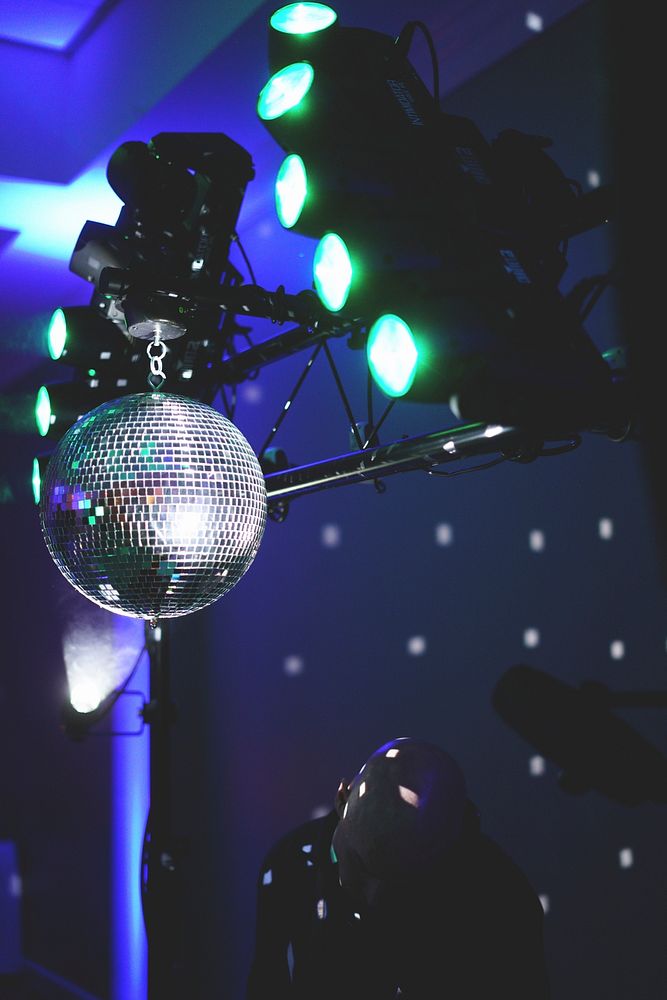 A bald man standing under a disco ball hanging from the spotlights. Original public domain image from Wikimedia Commons