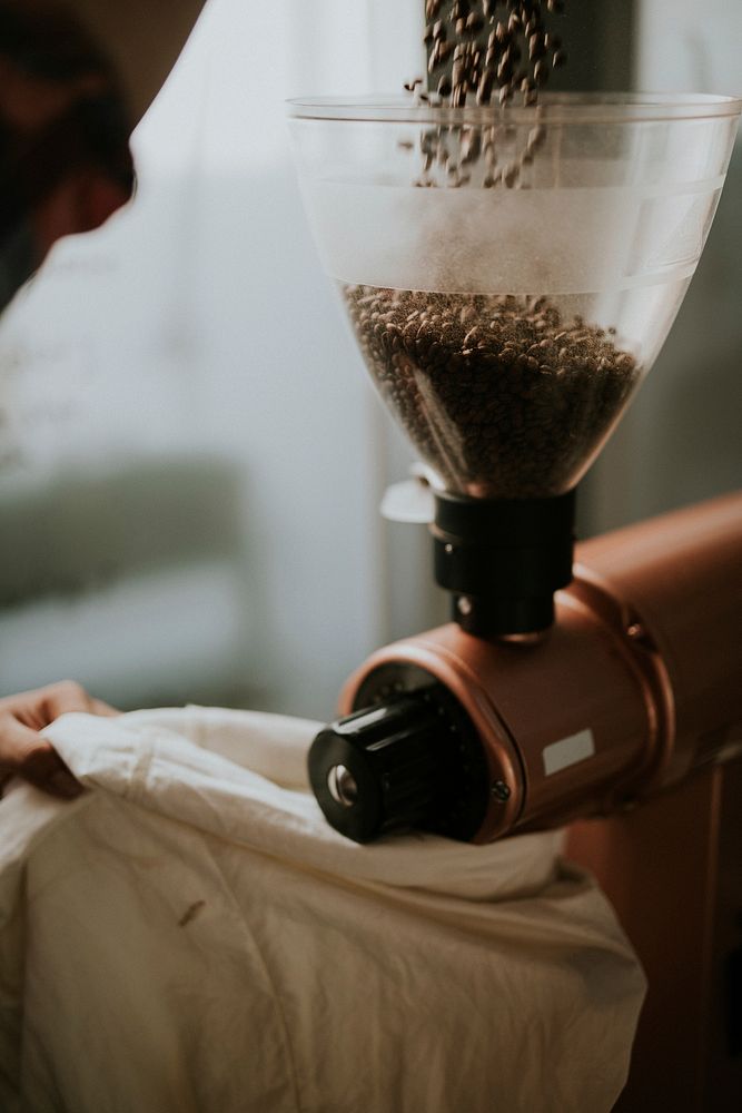 Pouring coffee beans into a grinder in a cafe kitchen. Original public domain image from Wikimedia Commons