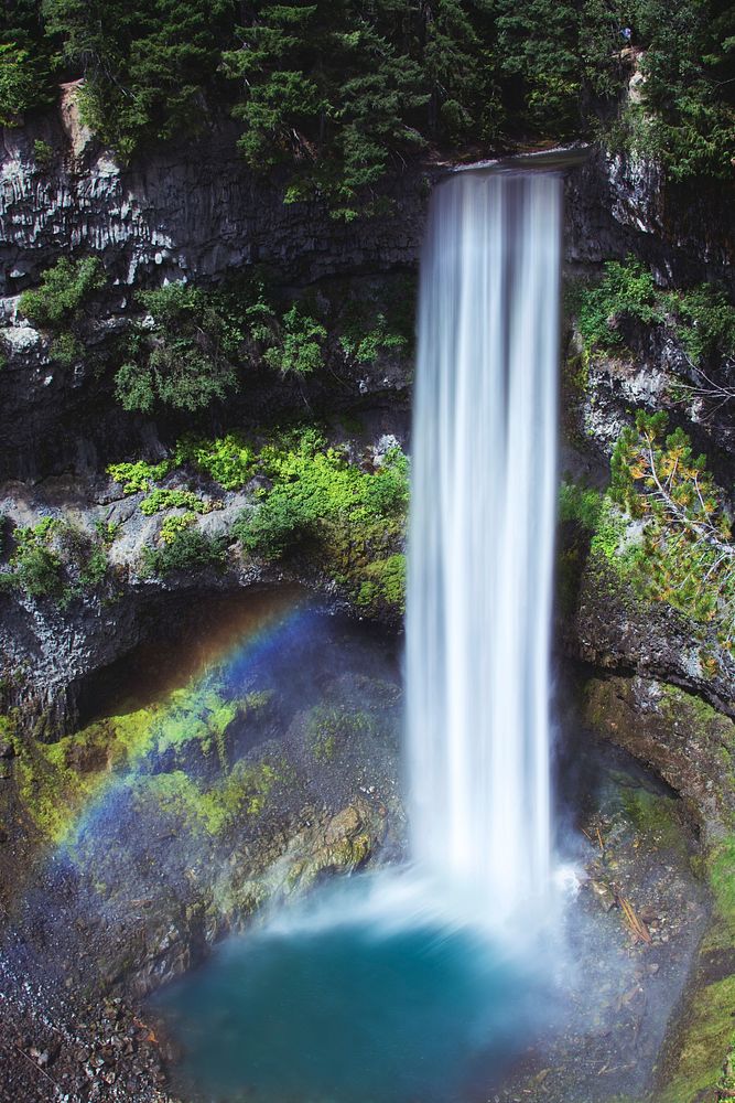 A massive waterfall flowing into a bright blue colored area with a rainbow in British Columbia. Original public domain image…