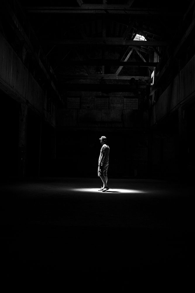 A dark black and white photo of a man standing in a building in Red Hook, Brooklyn, New York. Original public domain image…