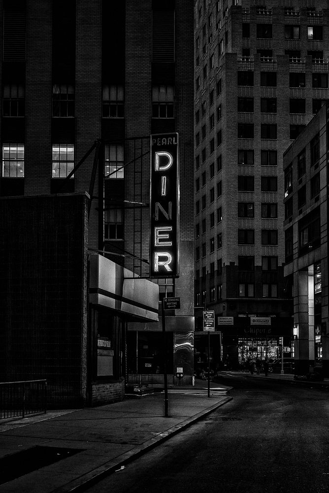 Black and white night shot of diner sign surrounded by city buildings in Financial District. Original public domain image…