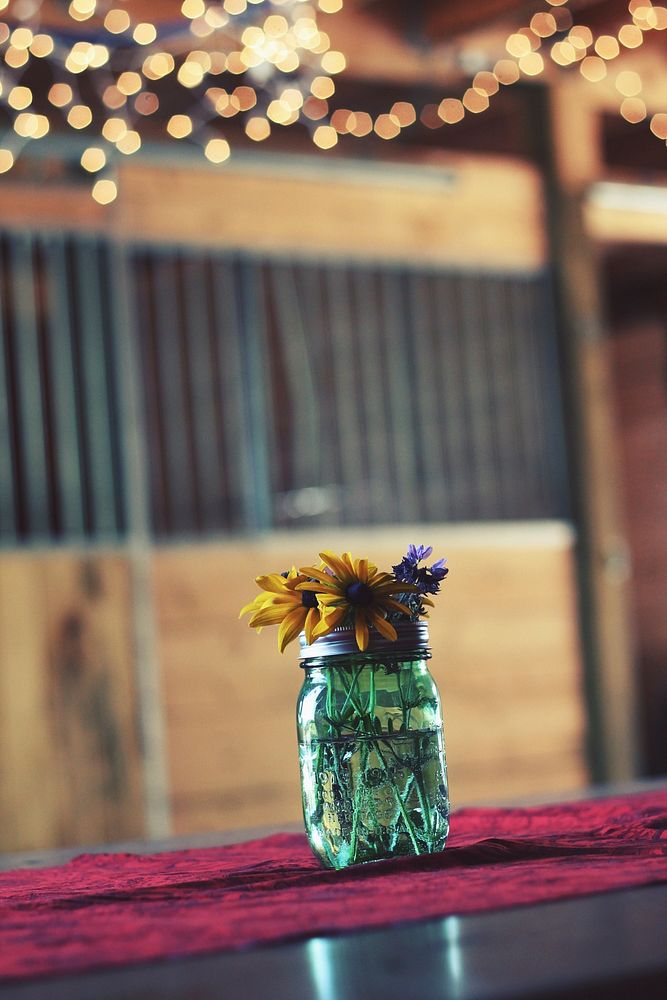 A glass jar with yellow and violet flowers on a wooden surface. Original public domain image from Wikimedia Commons