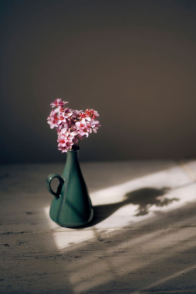 Small pink flowers in a green vase casting a shadow on a wooden surface. Original public domain image from Wikimedia Commons
