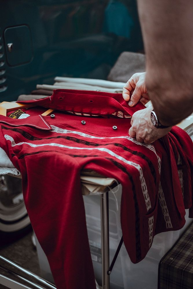 A person examines a red vintage garment on a table in Lewis Cubitt Square. Original public domain image from Wikimedia…