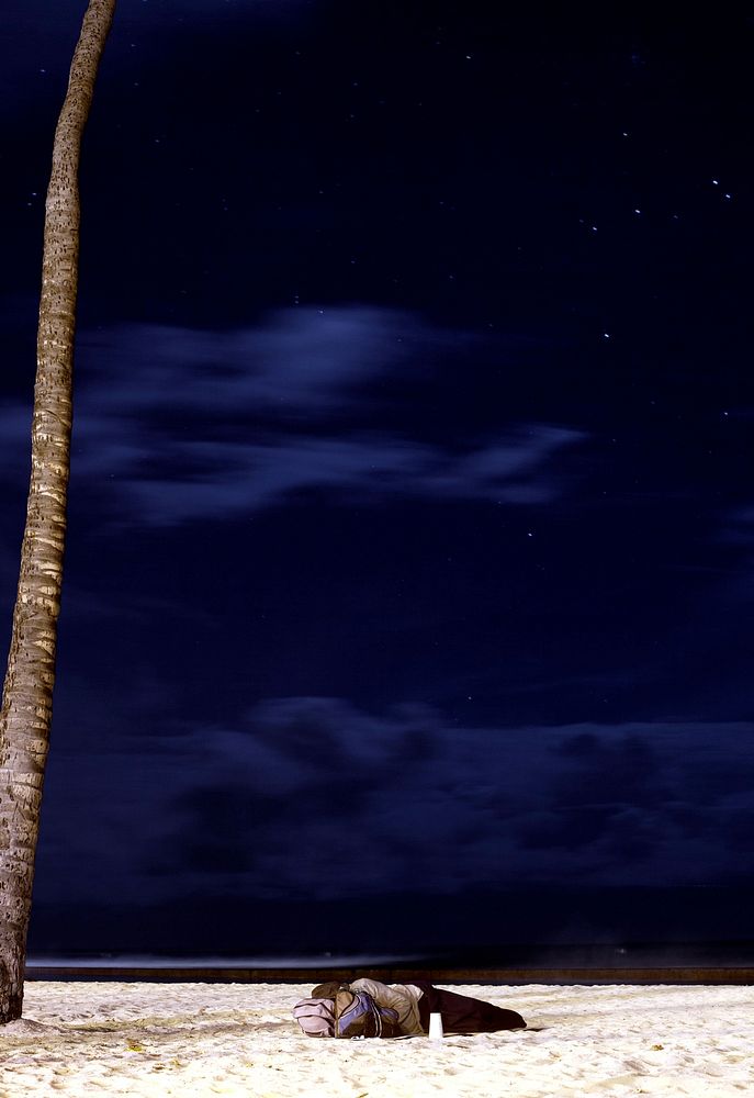 Person lying on the sand beach by the palm tree underneath the starry sky. Original public domain image from Wikimedia…