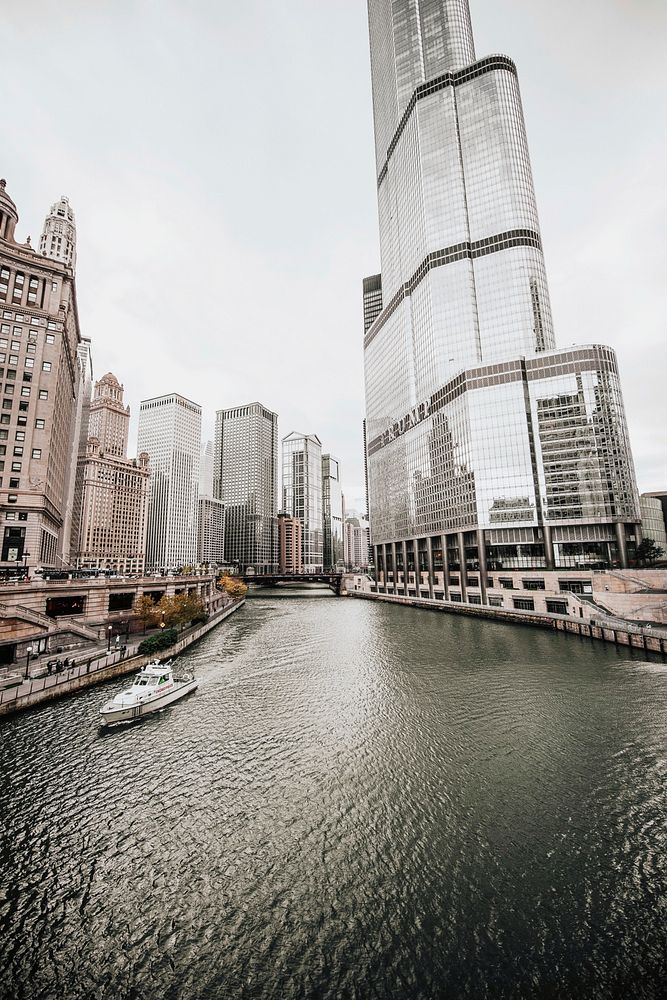 A pale shot of the Chicago river with a boat on it next to a skyscraper. Original public domain image from Wikimedia Commons