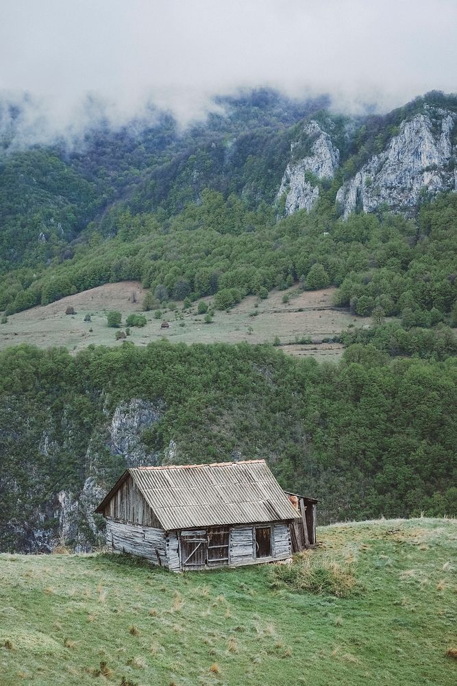 A dilapidated cabin on a grassy hill in the mountains. Original public domain image from Wikimedia Commons